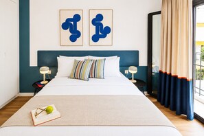 Een bed met een witte dekbedovertrek, gestreepte kussens en een boek met een bril op een witte vloerkleed.