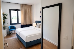 Een hotelkamer met een bed, een stoel, een kamerplant, een raam met gordijnen en een deur.