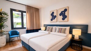 Uma cama de casal com cabeceira, duas luminárias de apoio, um vaso de planta, uma cadeira azul e uma janela com cortinas.