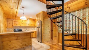 A wooden cabin interior with a kitchen, a central island, a spiral staircase, and a window with a view. - *Spacious 5BD w/ Hot Tub | FirePit + Fireplaces* (Sevierville)