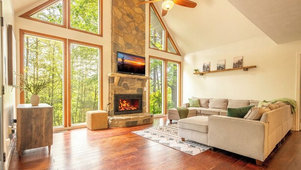 A spacious living room with a stone fireplace, large windows, a ceiling fan, and a sofa. - *Spacious 5BD w/ Hot Tub | FirePit + Fireplaces* (Sevierville)