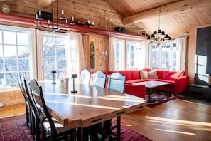 En inredning med träpanel, ett matbord, stolar, en röd soffa och en öppen spis.