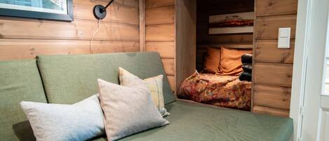 Interior d'una cabana de fusta amb un sofà verd, almoadines, un quadre amb marc i una làmpada.