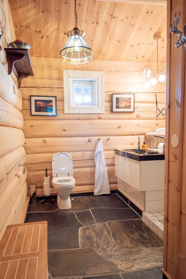 A log cabin bathroom with a toilet, sink, and hanging light fixture.