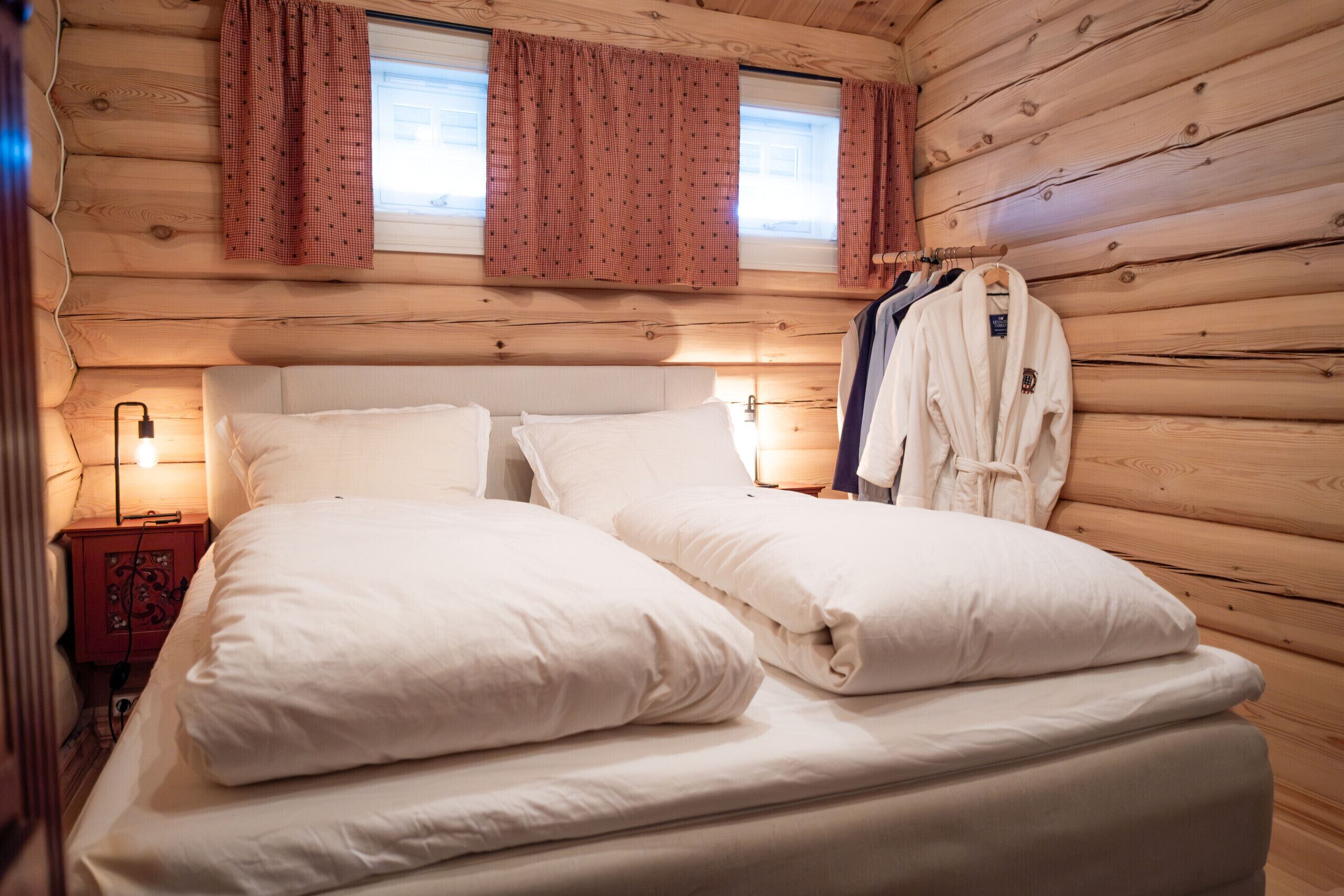 A wooden cabin-style room with a bed, two bedside tables, and a robe hanging on a rack.