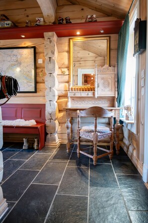A log cabin interior with a wooden chair, a bench, a map on the wall, and a wooden cabinet.