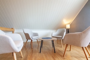 Een kamer met een schuine kap, een ronde tafel met stoelen en een lamp.