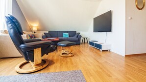Uma sala de estar moderna com uma poltrona de couro, um sofá, uma mesa de centro, uma TV fixada na parede e piso de madeira.