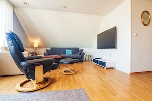 Een moderne woonkamer met een leren fauteuil, een bank, een salontafel, een aan de muur bevestigde televisie en een houten vloer.
