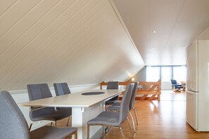 A modern interior with a white table, grey chairs, a wooden bench, and a white refrigerator.