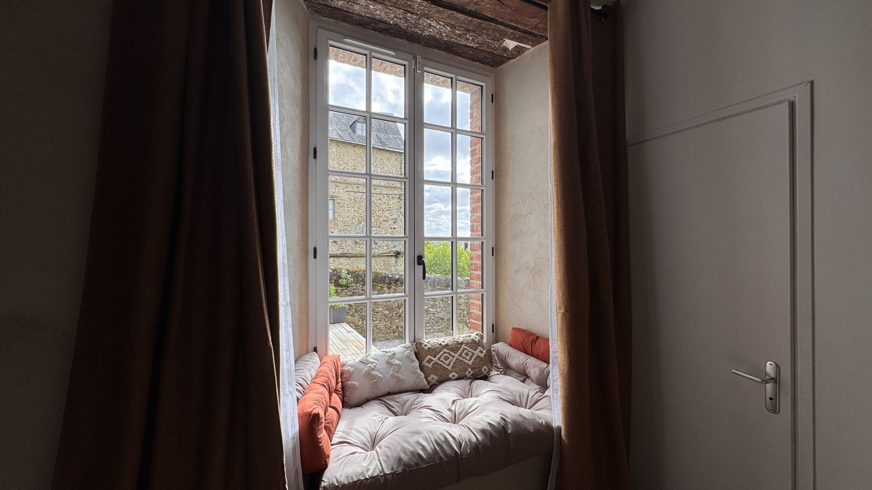 Ein Zimmer mit einem großen Fenster, einer gepolsterten Bank und einer Tür.