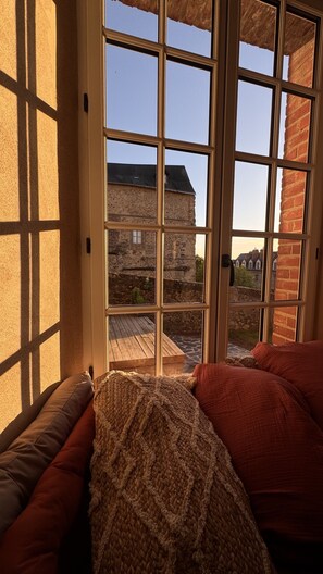 A room with a large window, a wooden bench, and a view of a brick building. - Maison Saint Christophe (Le Mans)