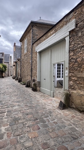 A cobblestone street with stone buildings, a garage door, and a stone wall with a number plaque. - Maison Saint Christophe (Le Mans)