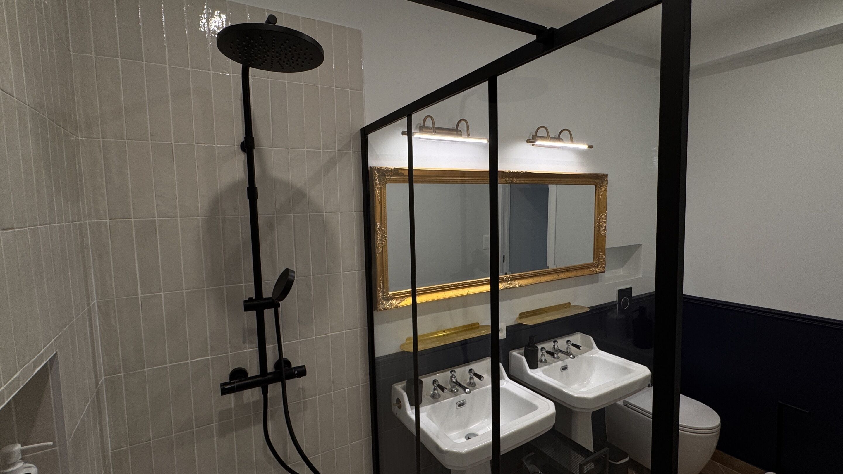 Une salle de bain avec une douche, deux lavabos, un miroir et des toilettes.