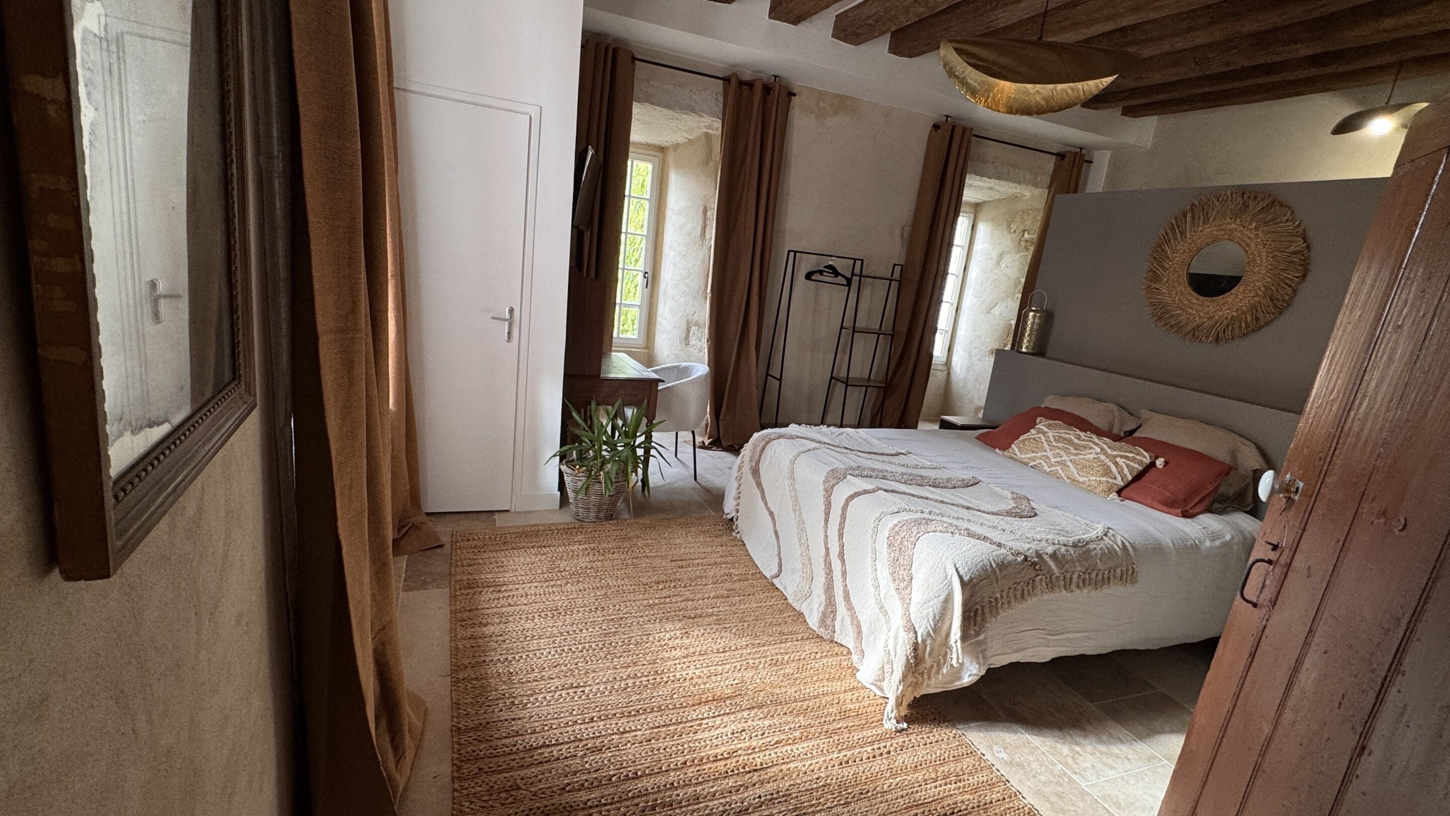 A bedroom with a bed, a desk, a chair, a potted plant, and a mirror.