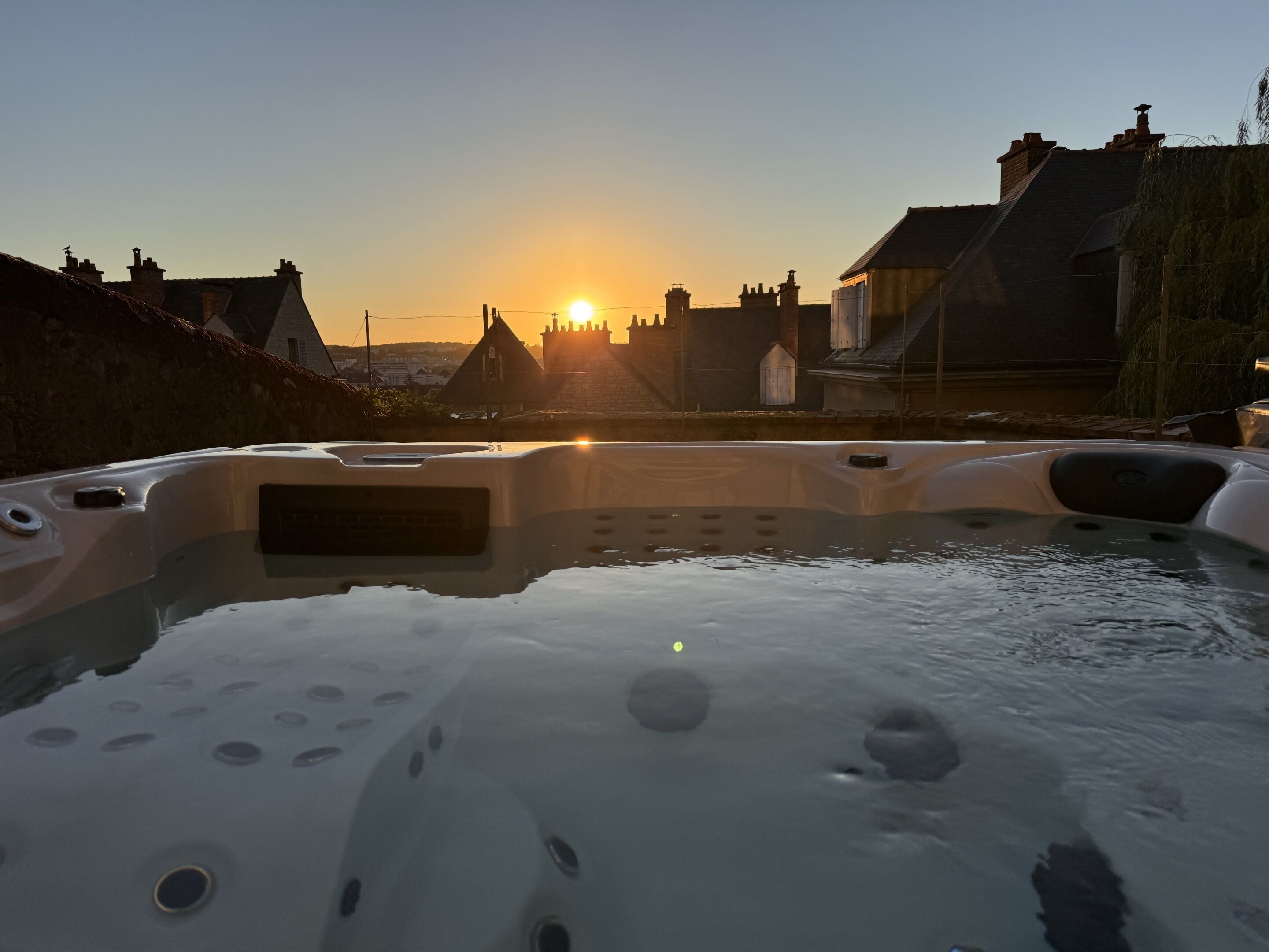 Uma banheira de hidromassagem com vista para um pôr do sol sobre uma área residencial.
