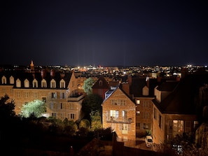 A nighttime view of a cityscape with illuminated buildings and a distant church spire. - Maison Saint Christophe (Le Mans)