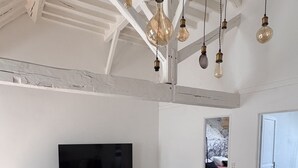En stue med en stor hjørnesofa, et fladskærms-tv og hængende lamper.