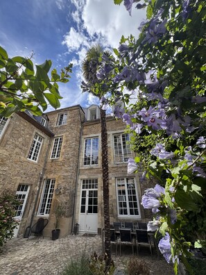 A stone building with multiple windows and a door, surrounded by greenery and flowers. - Maison Saint Christophe (Le Mans)
