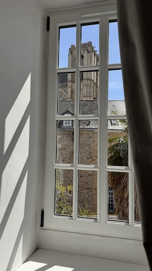 A window with a view of a historic building with stone walls and a tower. - Maison Saint Christophe (Le Mans)