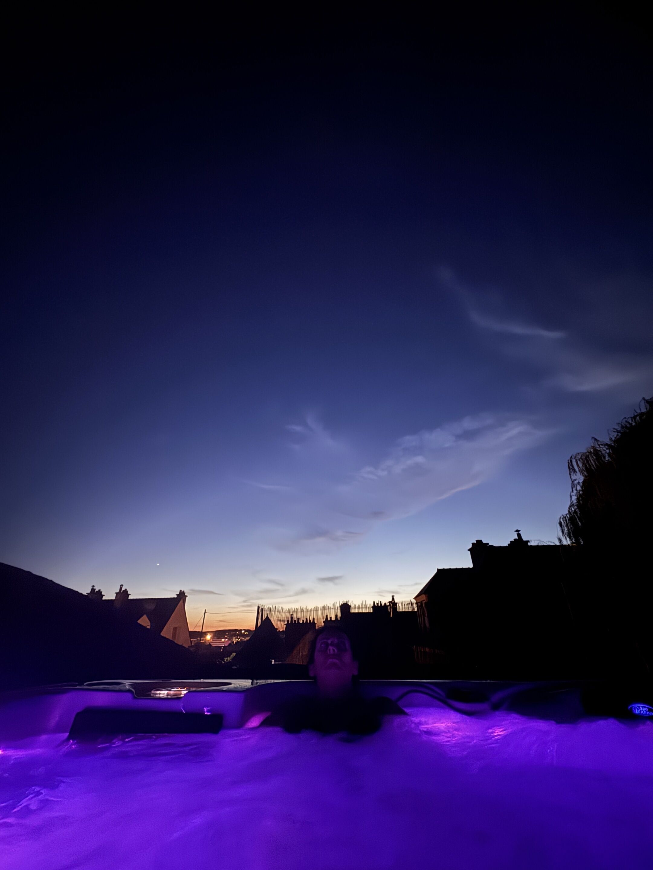 A person lying in a hot tub with a view of the sky and buildings in the background.