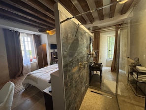 A modern bathroom with a shower, a toilet, and a sink. There is a bed with a window and curtains in the adjacent room. - Maison Saint Christophe (Le Mans)