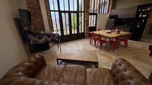 Un área de comedor con una mesa de madera y sillas rojas, una mesa de billar y vistas al exterior a través de grandes ventanales.
