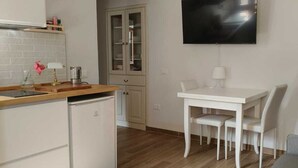 Een moderne keuken met witte kasten, een inbouwvaatwasser en een houten aanrecht. Er is een eethoek met een witte tafel en stoelen, en een flatscreen televisie aan de muur bevestigd.