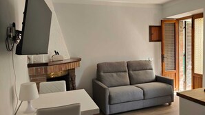 Een woonkamer met een bank, een tafel, een open haard en een aan de muur bevestigde televisie.