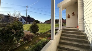 A covered porch with concrete steps leading to a white building, surrounded by a grassy area and a small stream. - Central loft with parking in Bergen (Bergen)