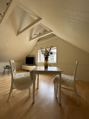A room with a sloped ceiling, a dining table with chairs, a TV, and a window with a view. - Central loft with parking in Bergen (Bergen)