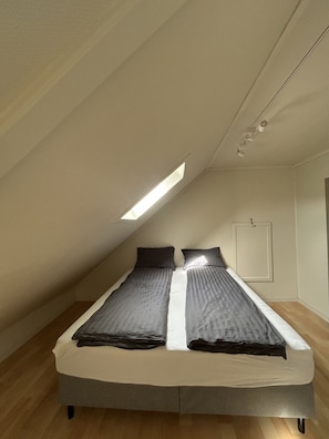 A bedroom with a sloped ceiling, a bed with grey bedding, a small window, and a door. - Central loft with parking in Bergen (Bergen)