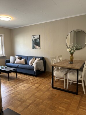 A living room with a blue sofa, a coffee table, a dining table with chairs, a mirror, and a framed picture on the wall. - Central 3 bedroom apartment with parking (Bergen)
