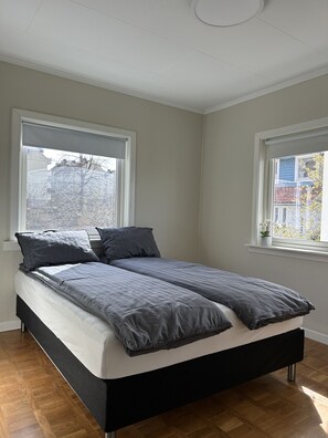 Un dormitorio con cama, dos ventanas y vistas a edificios.