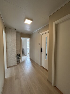 A hallway with a white brick wall, a door with a window, and a light fixture on the ceiling. - Central Apartment with parking, Bergen (Bergen)
