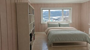 A bedroom with a bed, a window with a view, and a bookshelf.