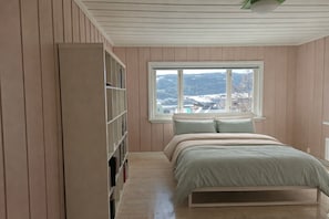 A bedroom with a bed, a window with a view, and a bookshelf. - Spacious Villa in Lillehammer (Lillehammer)