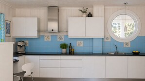 A modern kitchen with white cabinets, a round window, and blue tiles.