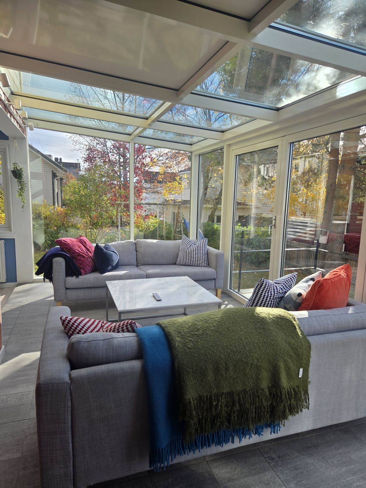 A conservatory with a grey sofa, a coffee table, and various cushions.