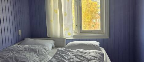 Een slaapkamer met twee bedden, een raam met gordijnen en uitzicht op bomen.