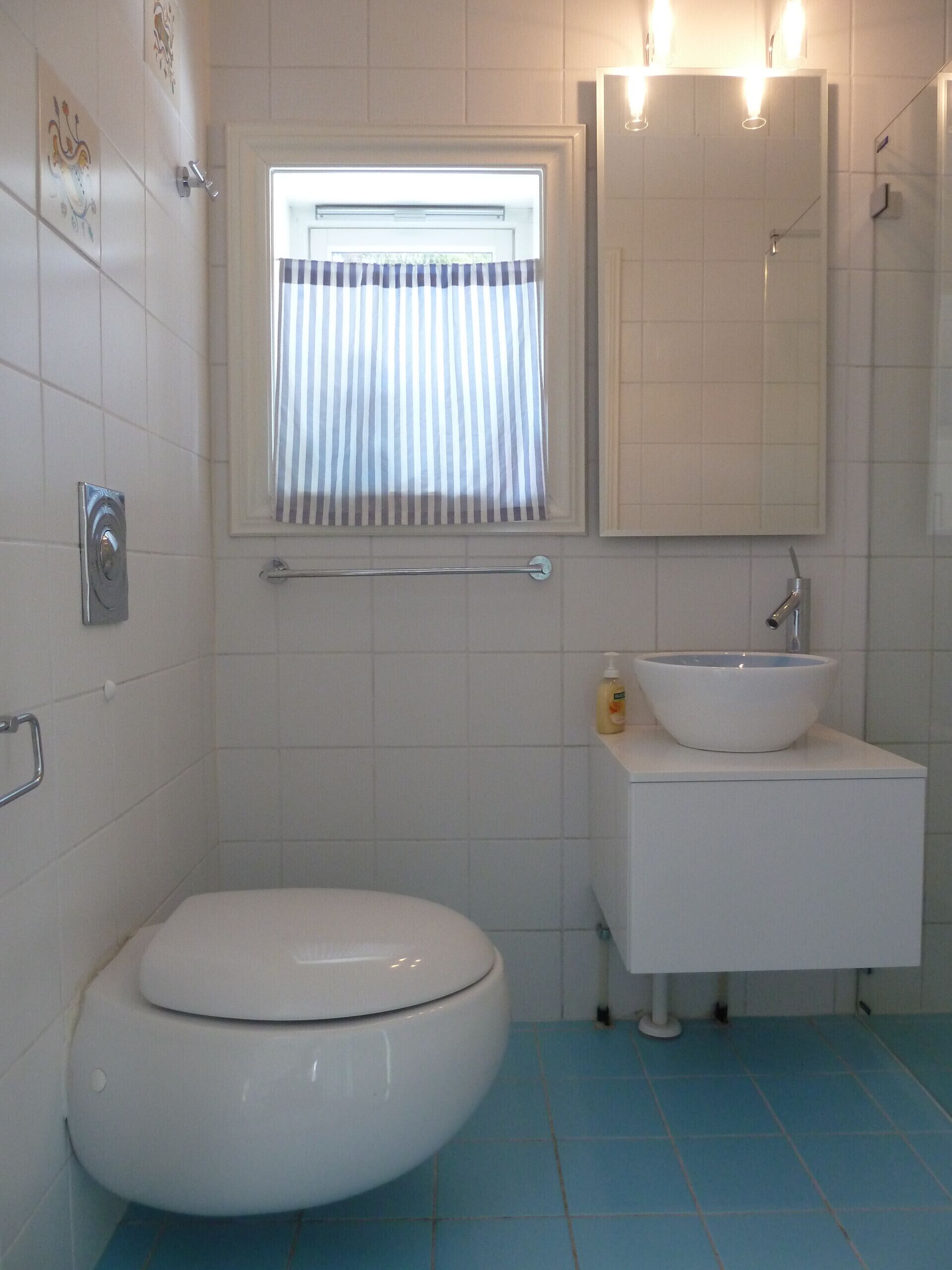 A bathroom with a toilet, a sink, a mirror, and a window with striped curtains.