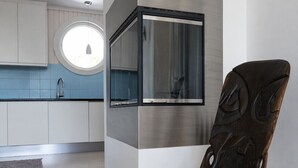 A modern kitchen with a built-in oven, a round window, and a dark wooden chair.