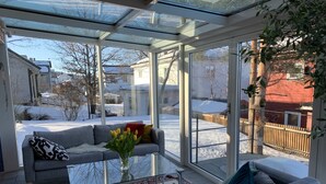 A conservatory with a glass ceiling, a grey sofa, a coffee table, and a vase with flowers.