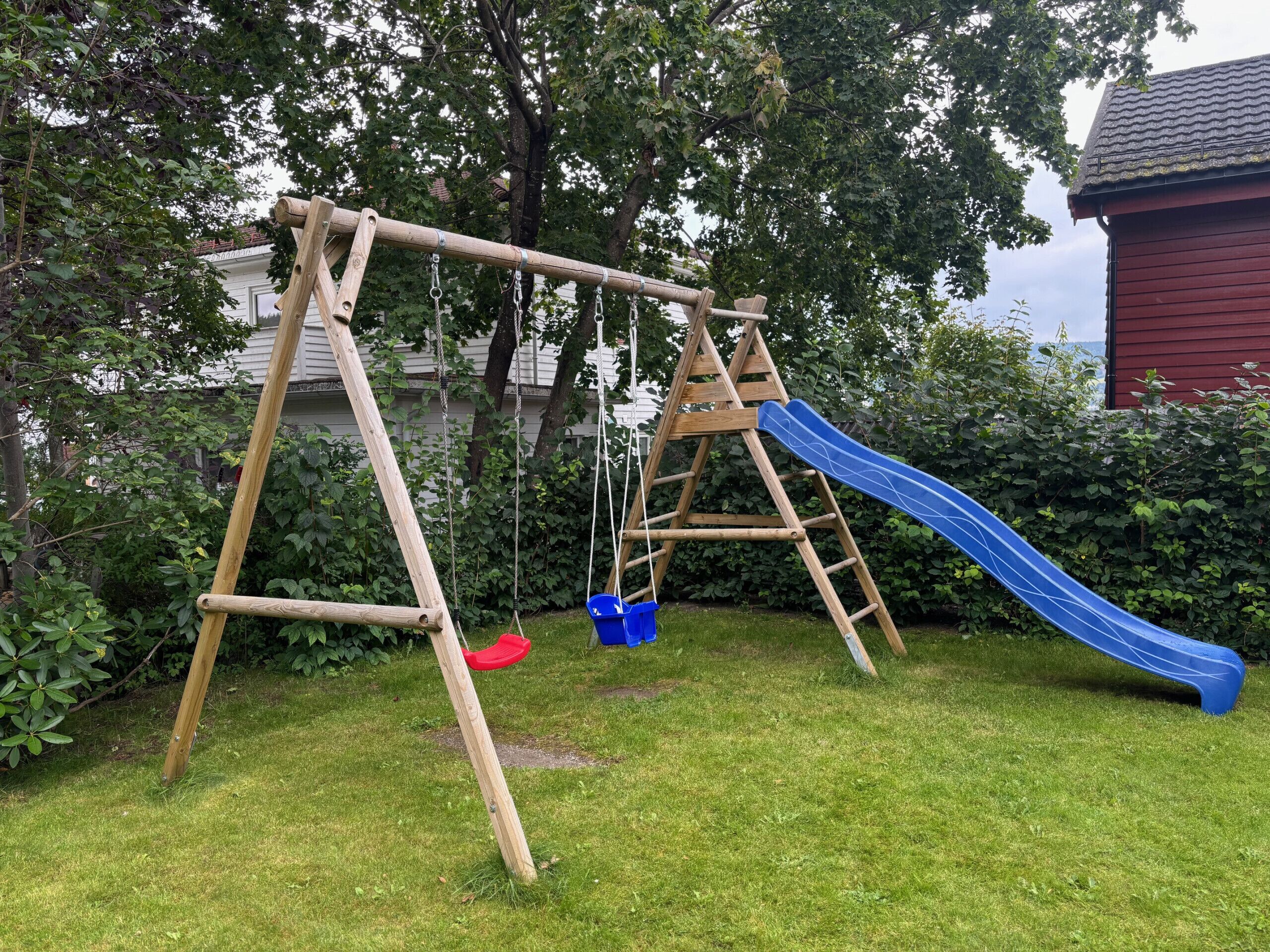 Ein hölzernes Schaukelgerüst mit einer blauen Rutsche auf einer Rasenfläche.