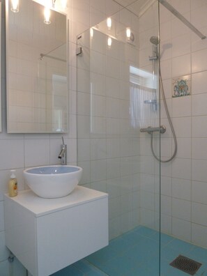 Une salle de bain avec un lavabo blanc, une douche en verre et un sol carrelé de carreaux bleus.