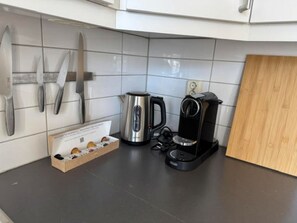 Ett kök med en kaffebryggare, en vattenkokare och knivar som hänger på väggen.