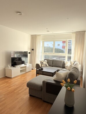 Ein modernes Wohnzimmer mit einem Flachbildfernseher, einem grauen Sofa, einem Couchtisch und einer Vase mit Blumen.