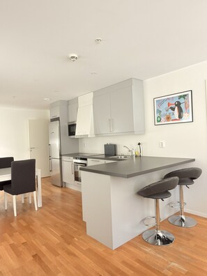 A modern kitchen with white cabinets, a stainless steel refrigerator, and a bar area with stools. - Central and spacious apartment in Bergen (Bergen)