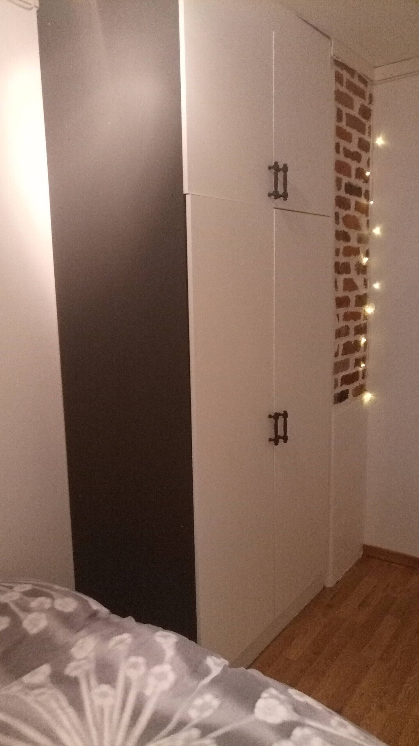 Une chambre avec un lit, une armoire et un mur décoré d’un motif en briques, agrémenté de guirlandes lumineuses.