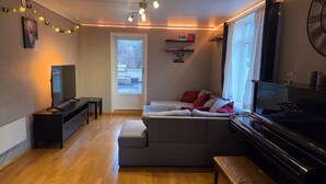A modern living room with a sofa, a TV, a piano, and a bookshelf. - Apartment with sea and mountain view (Bergen)
